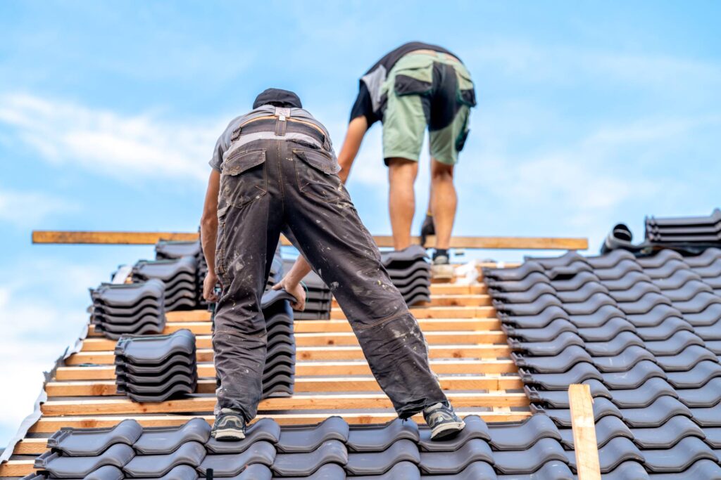 Two workers in protective gear installing roof tiles